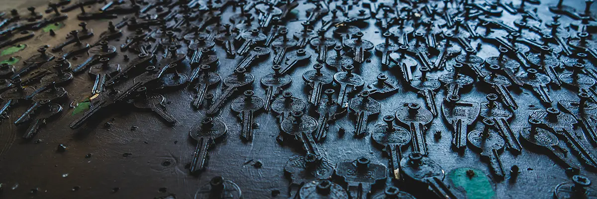 Viele dunkle Metallschlüssel, dicht nebeneinander auf einer Oberfläche befestigt, fotografiert aus schräger Perspektive.